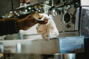 Close-up of a person cleaning a coffee machine using a cloth. Focus on hygiene and maintenance.