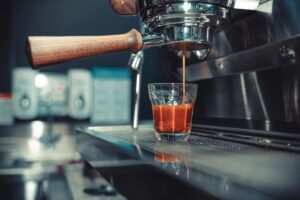 Espresso shot brewing from a machine with wooden handle in a modern cafe setting.